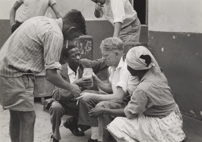 Black and white photograph by Ernest Cole showing Black South Africans receiving assistance from white officials in a segregated urban setting.