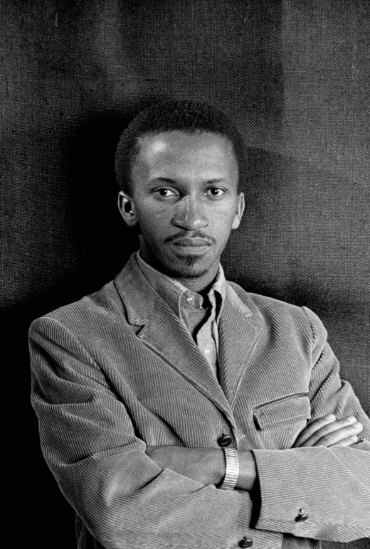 Portrait of Ernest Cole, South African photographer, photographed in the early 1960s with arms crossed against a dark backdrop.