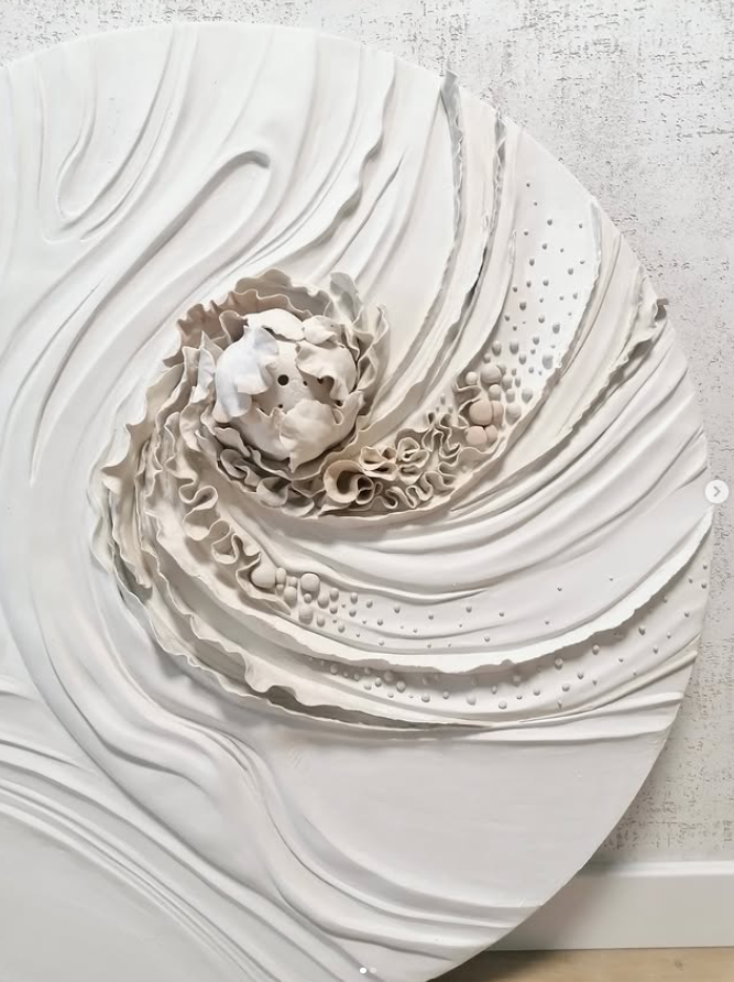 White circular sculptural relief with layered textures and organic central forms mounted on a wall