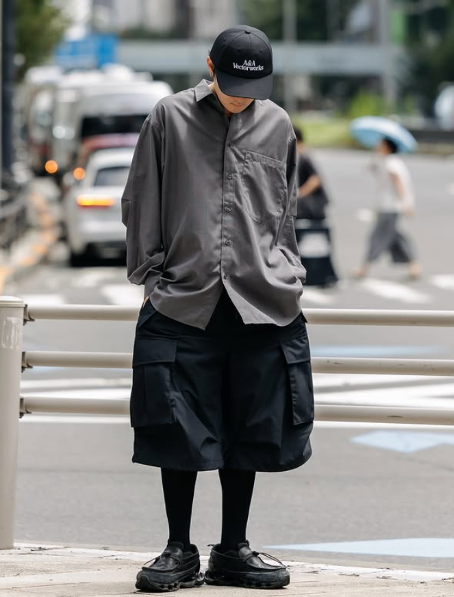Ryo Takashima in a monochrome grey outfit with layered shorts and black footwear, photographed on a city street in Tokyo