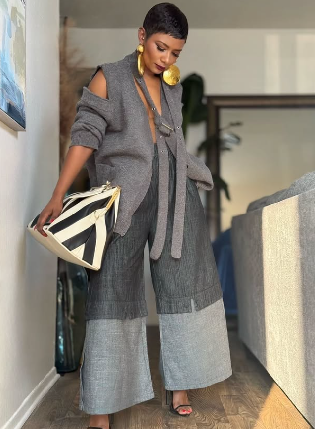 Kenya Freeman smiling in her design studio, wearing a black structured outfit surrounded by garments and patterns.