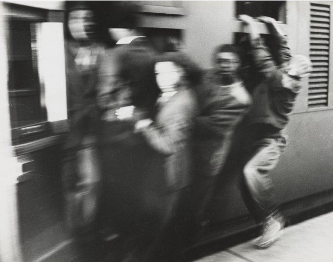Black and white photograph by Ernest Cole showing Black South Africans receiving assistance from white officials in a segregated urban setting.